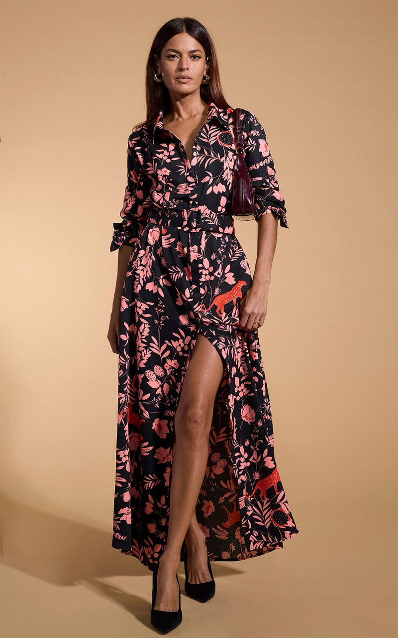 A female model faces forwards. She wears a Dancing Leopard maxi shirt dress. The dress is black with a orange flower print.