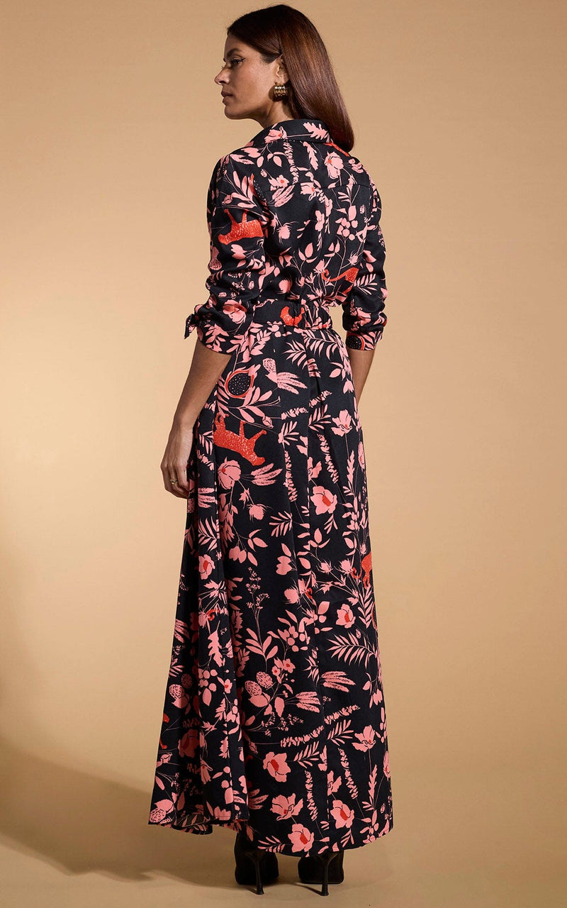 A female model faces backwards. She wears a Dancing Leopard maxi shirt dress. The dress is black with a orange flower print.