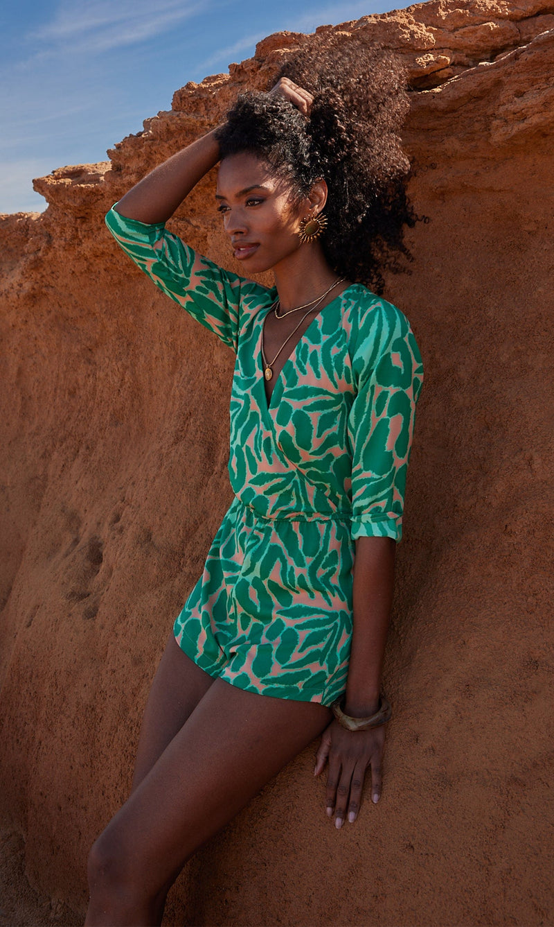 A female model faces forwards, leaning against a rock. She wears a Dancing Leopard green and peach, zebra print playsuit.