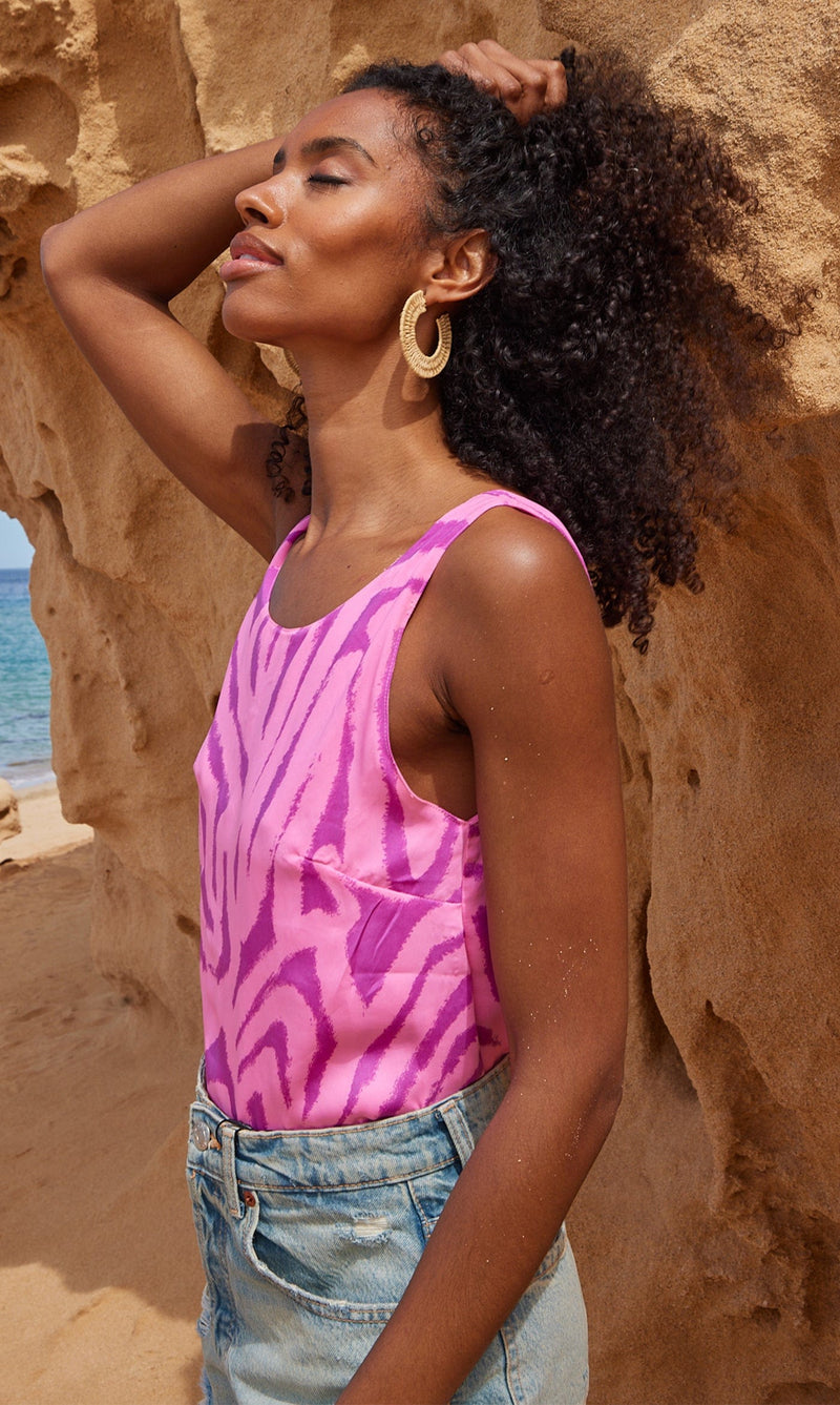 A female model faces forwards in front of a rock. She wears a Dancing Leopard pink, marble print top with denim shorts.