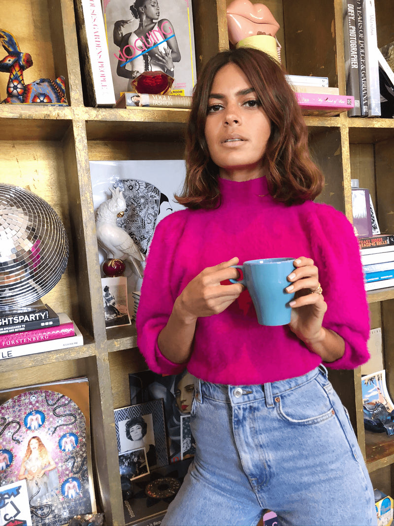 Dancing Leopard model wears felix jumper in cerise holding cup of tear against book shelf