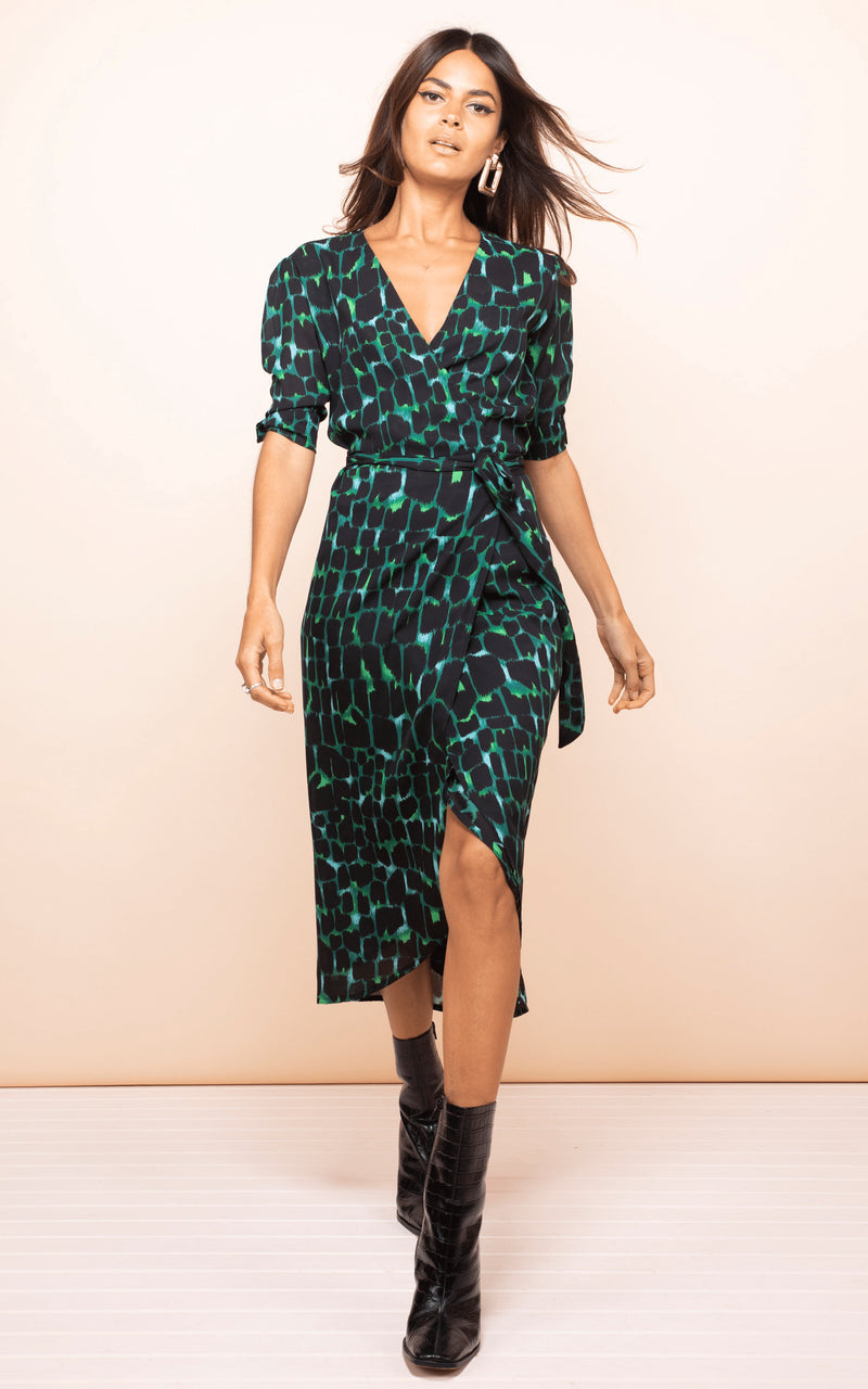 Brunette model walks forward wearing Olivera Midi Dress in green croc print with white boots