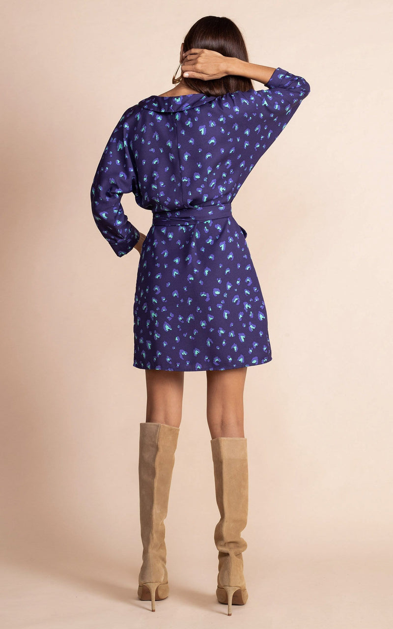 Dancing Leopard model standing back to the camera and wearing navy blue and purple mini wrap dress in leopard print, with tanned knee high boots