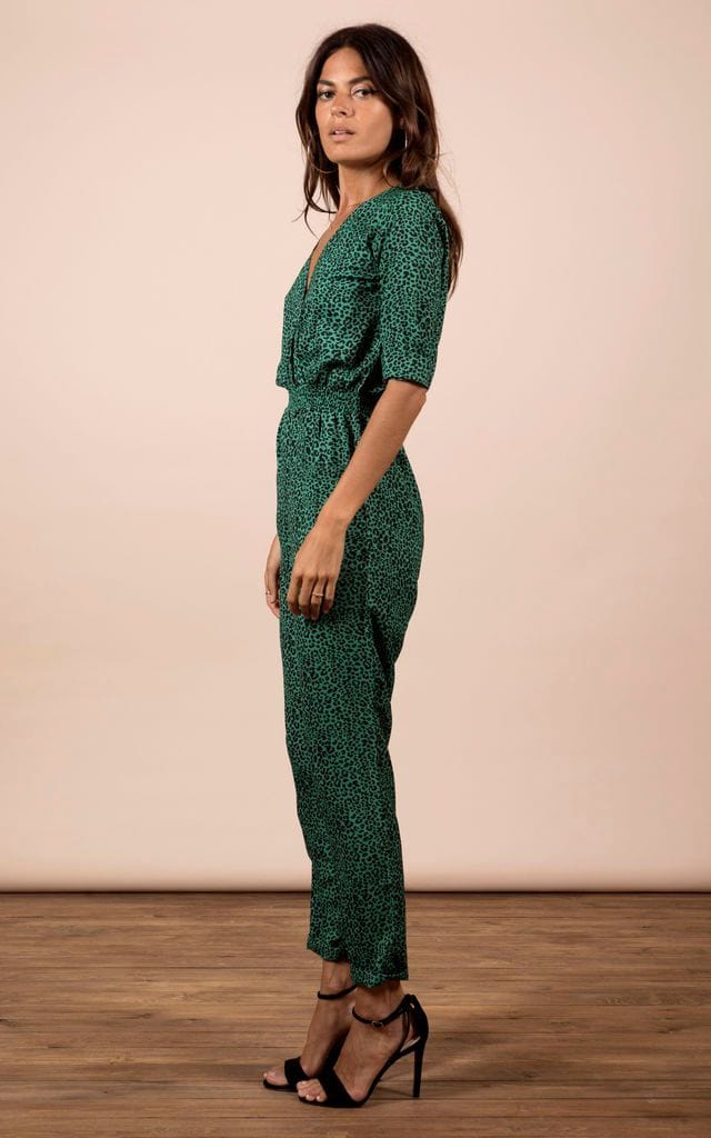 Brunette model faces sideways and looks at camera wearing Zion Jumpsuit in green leopard print