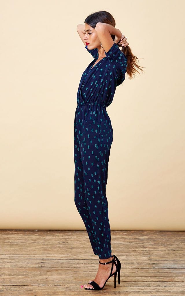 Dancing Leopard model faces sideways and holds hair wearing Zion Jumpsuit in navy cactus print with heels