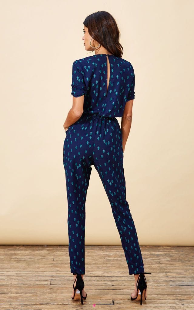 Backward-facing model wears Zion Jumpsuit in navy cactus print with heels